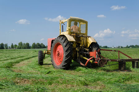 yellow red small tractor cutting the grass nice makes bend in the meadow  