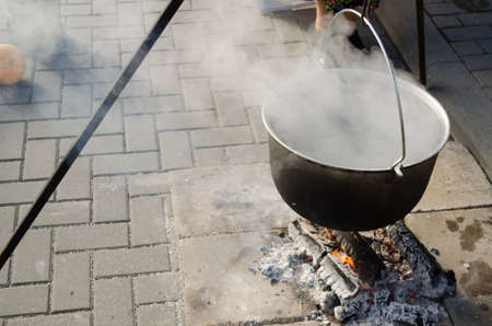 large antique old pot on metal rods strongly vaporize on fire outdoors の写真素材