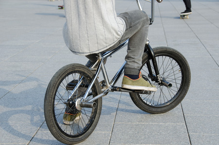 fragment of guy with sports clothing sit on sports BMX bicycle on grey urban concrete background 