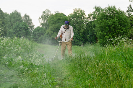 Worker man cut trim mow wet grass after rain. Water dew drops rise from meadow. の写真素材