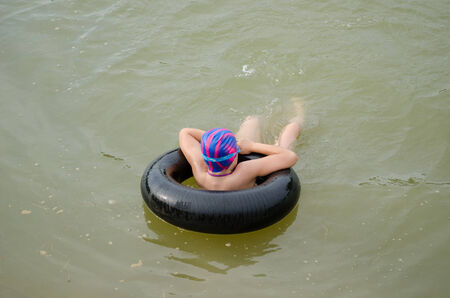 small girl with diving hat floating on an inflatable tire in water pond surface の写真素材