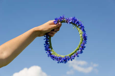 female hand hold summer nice cornflower crown in blue sky backgroundの写真素材