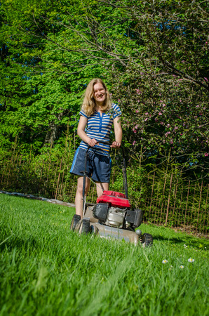 smiling country workwoman and fuel grass cutting machine in garden seasonal work の写真素材