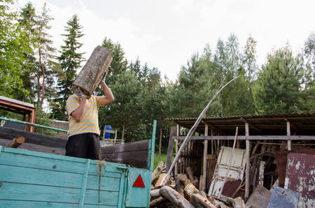 worker man unload tree log firewood wood from tractor trailer near rural woodshed house. の写真素材