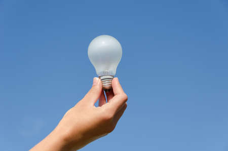hand holding an incandescent light bulb on blue sky background の写真素材