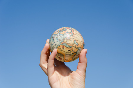 stylized global earth miniature in hand on blue sky background, environment control concept の写真素材