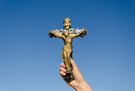 symbol of christianity metal cross with the crucified christ in woman hand on blue sky background の写真素材
