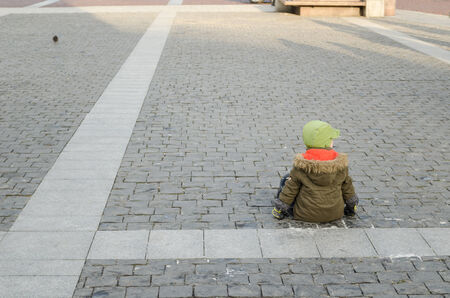 lonely child with thick jacket sit on the pavement in old town の写真素材