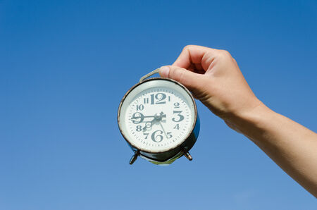 girl hand hold small old retro alarm clock with large black numerals on blue sky background の写真素材