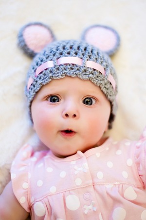 baby girl lying on her back and smiling on the bed in pink clothes and hat with ears