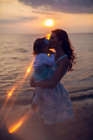 mother holding her child at sunset by the seaの写真素材