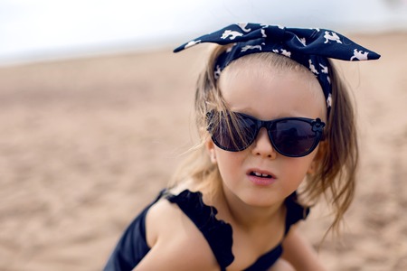 a little girl stands on the shore of the beach in a black bathing suit and black glassesの写真素材
