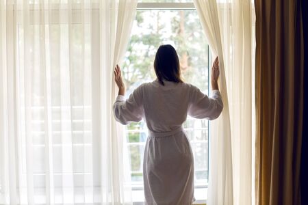 the girl standing at the window his back in a white Terry robe and opens the curtainsの写真素材
