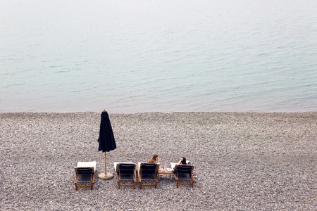 Sochi, Russia - April 23: two girls lying on the sunbeds on the beach with pebbles by the sea with closed black umbrellas and eat on April 23, 2016のeditorial素材
