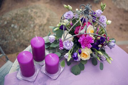 decor design small round table on the nature of the sea with purple lilac tablecloth thick candles and flowers in a cage with rosesの写真素材