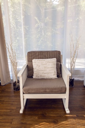 white rocking chair with brown cushion in the interior against white curtainsの写真素材
