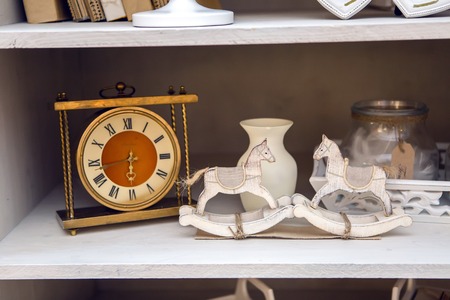 white outdoor small cupboard with trivia books, clock, wooden horses, jars, candle holders, photo framesの写真素材