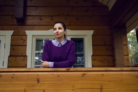 young girl in a purple sweater and black jeans out on the porch of a wooden houseの写真素材
