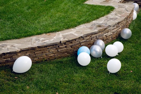 balloons lying on green grass with a barrier of stone in the gardenの写真素材