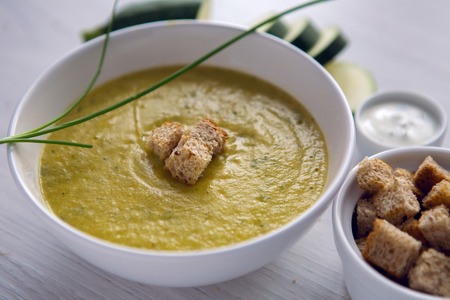 zucchini soup on a white wooden table with croutons in a bowl and sour cream in a Cupの写真素材