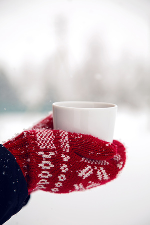 hands in red mittens holding a mug of tea while the snow in the winterの写真素材