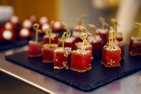 red fish on wooden skewers with the sesame seeds on a black trayの写真素材