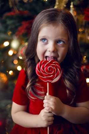 little girl three years in a red dress licks a great round colorful candy
