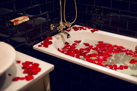 petals of red roses in a white bathroom with black tiles and gold tapsの写真素材