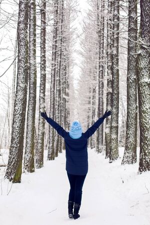 girl in the blue jacket and the cap raised on the upper arm in a grove of trees with high and snow-covered trees in winter.の写真素材