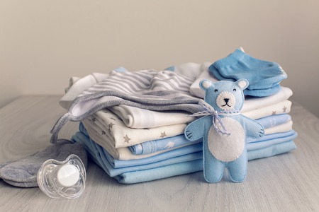 baby clothes with diapers are stacked with a pacifier and a toy bearの写真素材