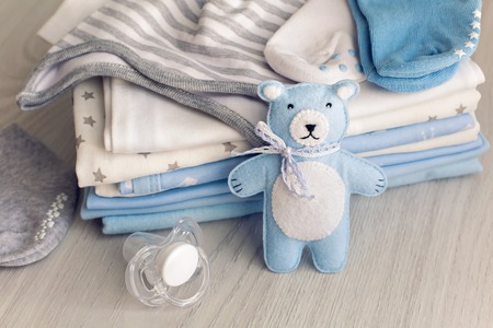 baby clothes with diapers are stacked with a pacifier and a toy bearの写真素材