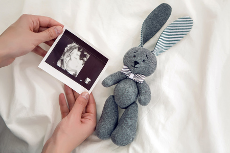 pregnant woman sitting on white bed and holds ultrasound babyの写真素材