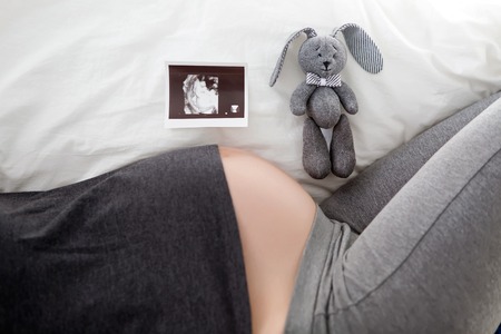 pregnant woman lies on white bed and ultrasound babyの写真素材