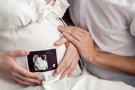pregnant girl holding with their hands the belly and the husband keeps the hand in the ultrasound of...