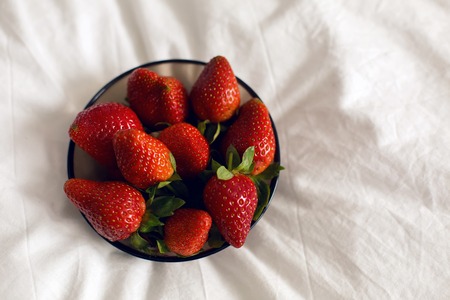 black transparent plate with fresh strawberries on a white bedの写真素材