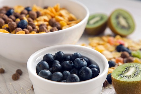 granola with blueberries in white bowl on wooden white background