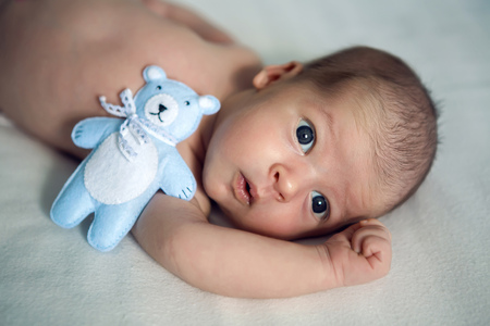 newborn lies with the blue soft toy bear on the bed on her backの写真素材
