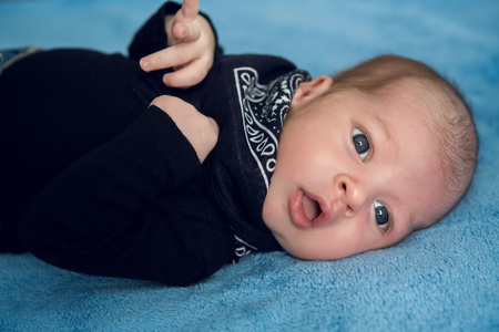 newborn baby lying in blue jeans and a black scarf on the neck on the gray bedの写真素材