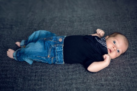 newborn baby lying in blue jeans and a black scarf on the neck on the gray bedの写真素材