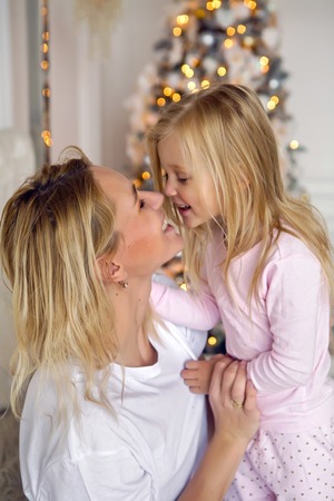 mother sitting with her daughter on the big bed and standing next to Christmas treeの写真素材