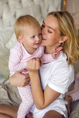 mother sitting with her daughter on the big bed and standing next to Christmas treeの写真素材