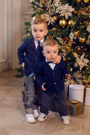 two young brothers in suits standing next to the Christmas tree