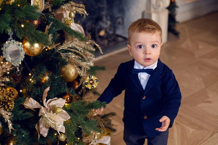 baby boy stands in a suit at Christmas at Christmas tree with giftsの写真素材