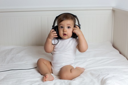 baby boy in big headphones in white big bedの写真素材