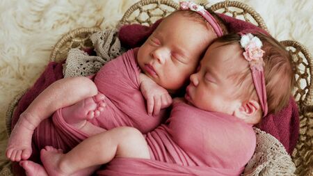 twins sisters newborn in the winding and in a basket on white fur backgroundの写真素材