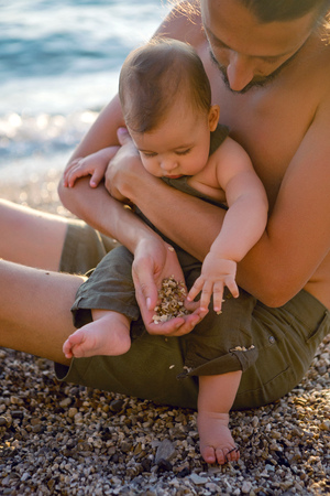father and son on the sea in shorts during sunset on the pebblesの写真素材