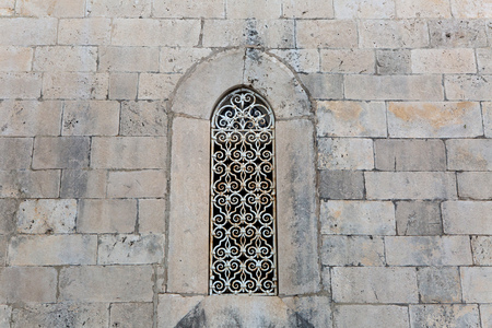 large window with carved iron bars in the old brick building of light stone
