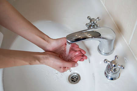 girl washes her hands in a white sink and a silver tapの写真素材