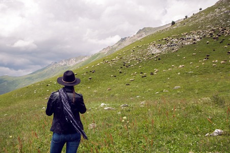 girl shepherd standing in the mountains in a meadow in a hat with sheep