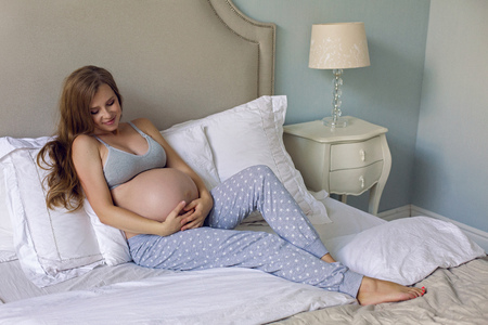 pregnant girl in bra and pants sitting on bed in studioの写真素材